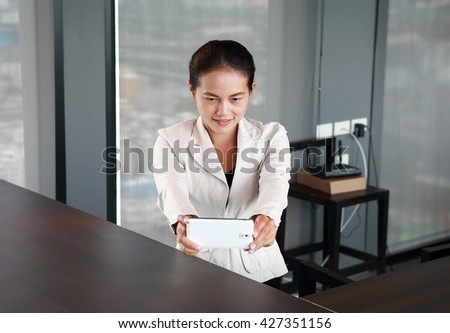 Young businesswoman sitting at the table on workplace in office using the smartphone taking pictures of herself 