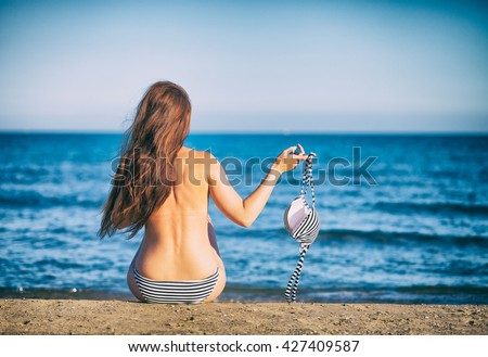 Beautiful woman on the beach in topless holding bikini
