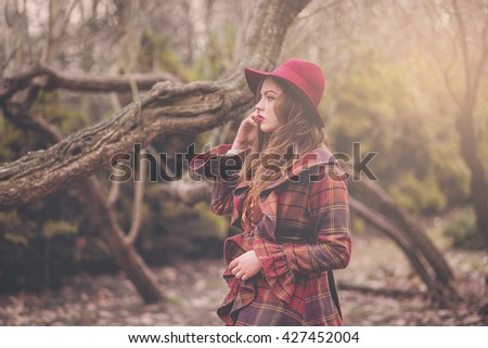 Elegant stylish beautiful young woman in a vintage hat burgundy color and the old English coat walks on cold spring park, fashion, style