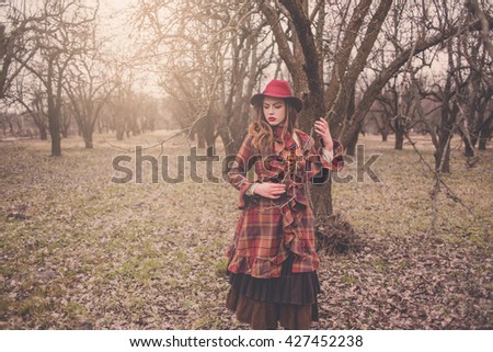 Elegant Fashionable beautiful young woman in a vintage hat burgundy color and the old English coat walks on cold autumn park, fashion, style