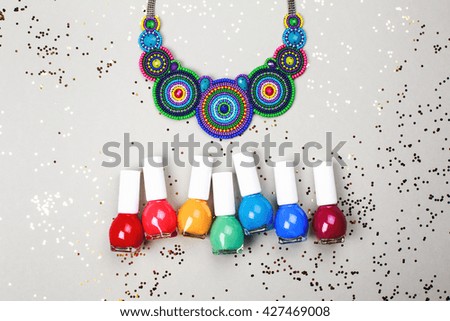 Beautiful multicolored necklace and rainbow of Nail Polishes lying on grey festive background.