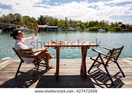 Beautiful woman taking selfie and enjoys the coffee and cake on a river pier