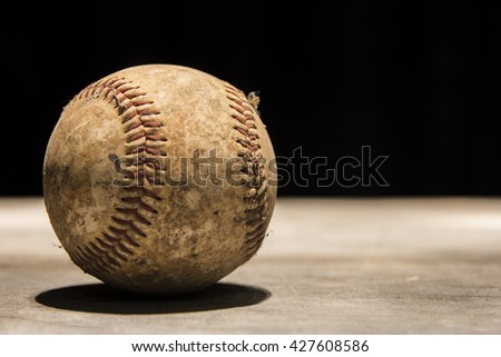 An old, vintage, worn out baseball on a black background.
