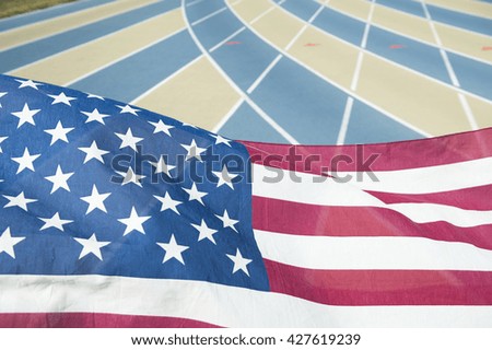 Bright red white and blue stars and stripes American flag flying over the lanes of an athletic running track