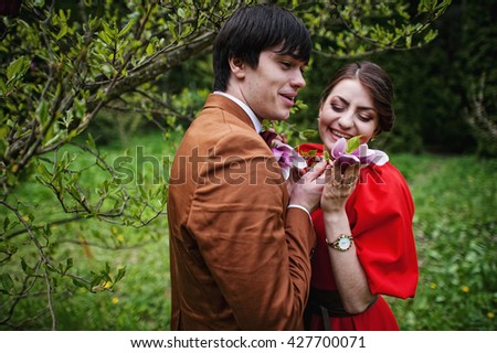 Couple hugging in love near magnolia tree. Stylish man at velvet jacket and girl in red dress in love together