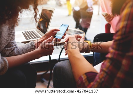 Closeup of woman is reading text message on mobile phone in network, while is sitting with laptop computer in co-working cafe. Group of friends are using gadgets during recreation time in coffee shop  Royalty-Free Stock Photo #427841137