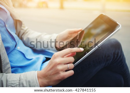 Closeup image of woman is watching photos on portable touch pad during her recreation time in weekend. Closely of hipster girl is using touch screen digital tablet while sitting in the park outdoors