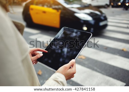 Closely image of woman`s hand is holding portable digital tablet with copy space screen for your advertising text message or promotional content, while is standing on the street near road pedestrian