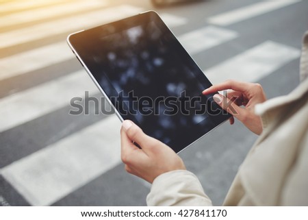 Closely image of woman`s hand is holding digital tablet with copy space screen for your advertising text message or promotional content. Female is using touch pad for navigation during walking outdoor