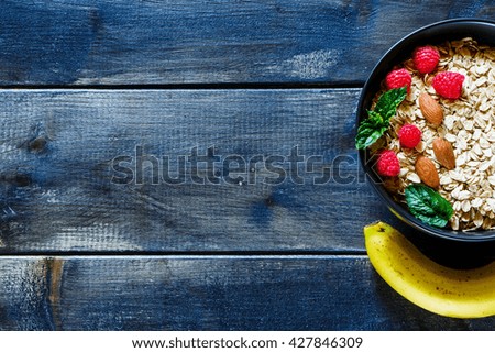 Oat flakes with fresh berries, nuts and banana in black bowl. Balanced breakfast ingredients on rustic background, top view, border. Healthy lifestyle and diet food concept. Flat lay. Copy space