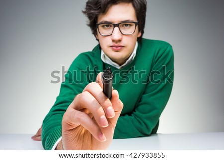 Concentrated young man in green pullover sitting at desk and writing something with marker