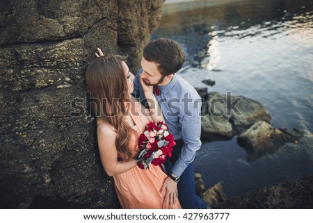 Wedding couple kissing and hugging on rocks near blue sea