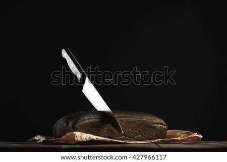 Big chief knife stuck inside homemade luxury bread from figs and rye in craft paper on rustic wooden table isolated on black