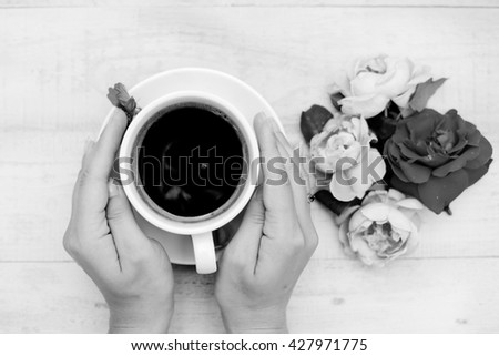 Black white photography top view hands with cup of coffee and rose petals beside
