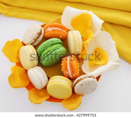 Plate with fresh macaroons and rose petals on light background