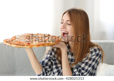 Happy young woman holding hot pizza at home