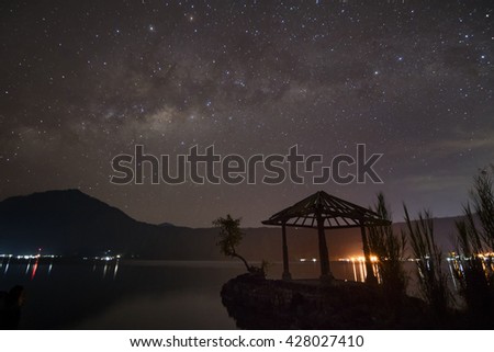 Milky way, a starry night sky over a lake.  Gazebo at foreground and mountain at background.  Location in Bali.