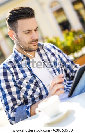 Handsome young man drinking coffee and listening to music on a smart phone