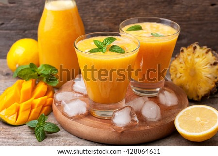 Tropical lemonade with mango, pineapple and mint in glasses and bottle on old wooden background Royalty-Free Stock Photo #428064631