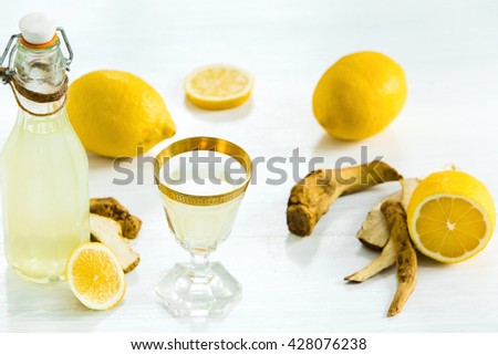 Home ginger tincture in a glass and fresh lemons on the white wooden background