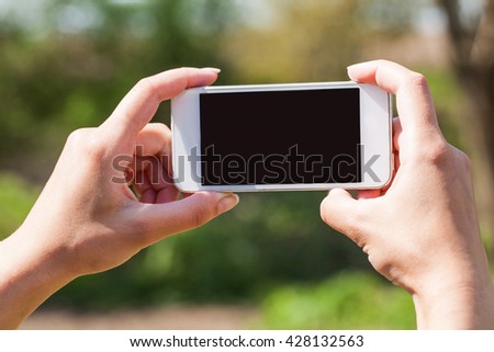 Woman holding smart phone in hand against green spring background. Blank screen with copyspace. Outdoor, in the park, summer.