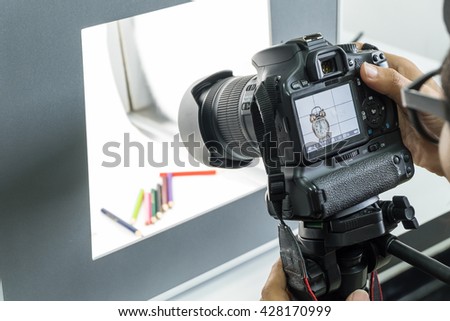 Photographer working on DSLR camera to shooting vintage alarm clock  and coloring pencils in lightbox