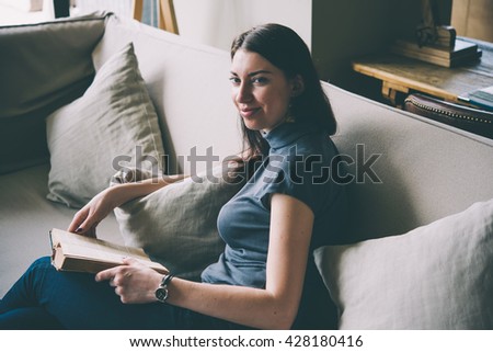 Young beautiful woman enjoys reading sitting on a comfortable couch. Learning and knowledge concept. Toned picture