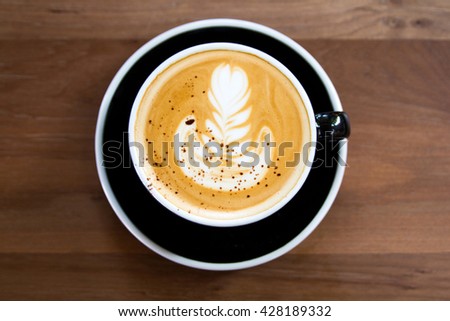 Cup of latte art coffee with froth flower put on black plate and wooden background.