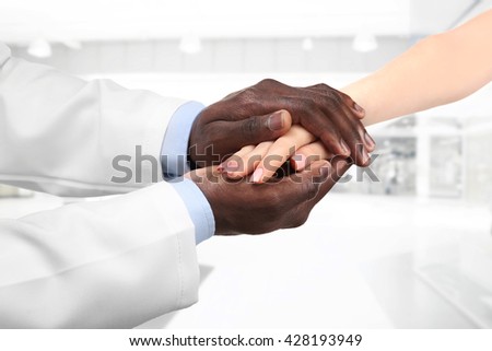 Male doctor holding patient's hand, on blurred background