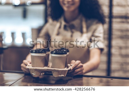 Best coffee to go! Part of young cheerful African woman in apron holding coffee cups while standing at cafe Royalty-Free Stock Photo #428256676