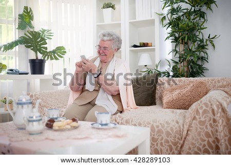 Old woman smiling and looking pictures on her smartphone