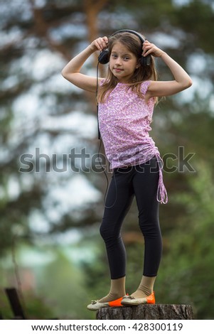 Little girl in headphones standing on a stump.