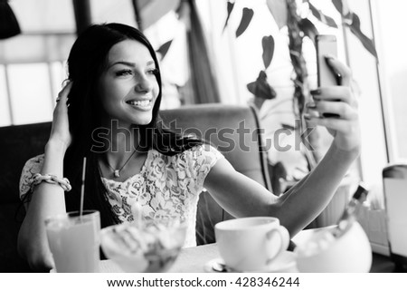 Portrait of beautiful brunette young lady making selfy picture on mobile cell phone having fun happy smiling on restaurant background