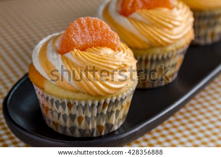 Row of orange and vanilla bean swirled cupcakes on black tray plate sitting orange gingham checkered background