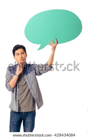 Handsome pensive young Chinese man is holding speech bubble, looking at it and thinking, isolated on white background