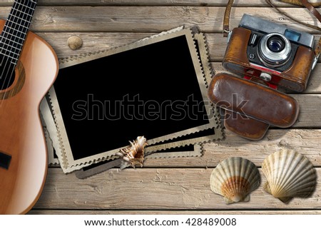 Vintage camera with leather case, acoustic guitar, a group of empty photos frames and seashells on a wooden boardwalk with sand