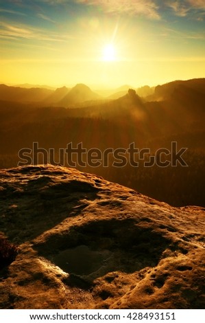 Sunrise in a beautiful mountain of Czech-Saxony Switzerland. Sandstone peaks increased from foggy background, the fog is orange due to sun rays. 