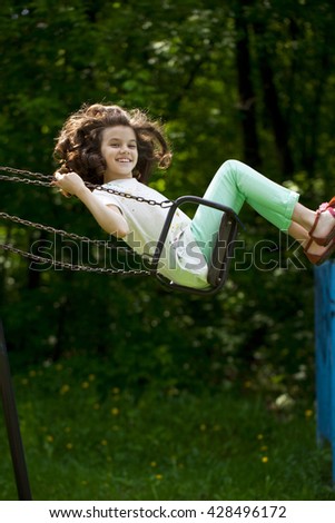 Happy Little girl on a swing in the summer park