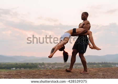 Beautiful dance. Mixed race gymnastic couple dancing on the pink sunrise in mountains