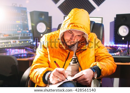 DJ writes new lyrics in recording studio. Young man in yellow coat wtites lyrics in recording studio.  DJ create new music track.