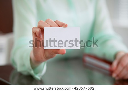 Business woman hands in a green blouse sitting at a desk in an office and holds out business card.