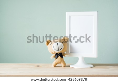 smiling bear with blank white picture frame on wood table with pastel color tone wall