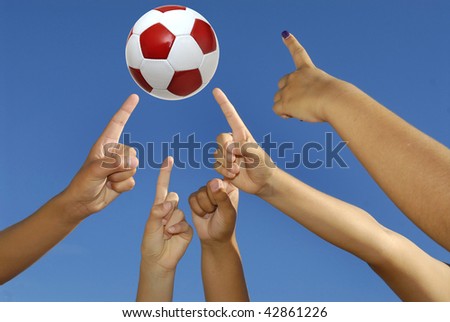 Several hands pointing up towards a soccer ball against the sky
