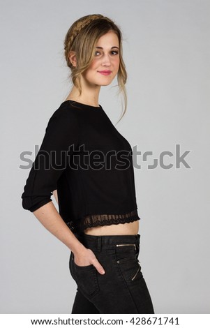 Beautiful blond girl with blue-green eyes on a white background. She wears a black t-shirt and a black trousers. 
