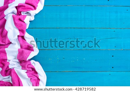Blank rustic teal blue wood beach sign with pink and white striped beach towel border; background with painted copy space 