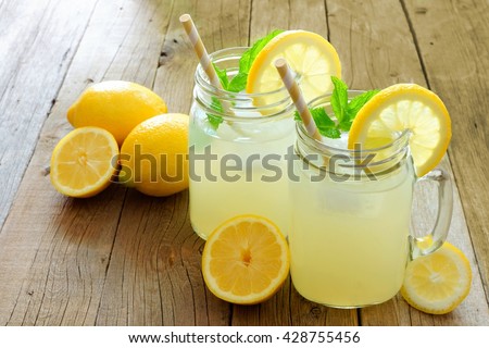 Two mason jar glasses of homemade lemonade on a rustic wooden background Royalty-Free Stock Photo #428755456