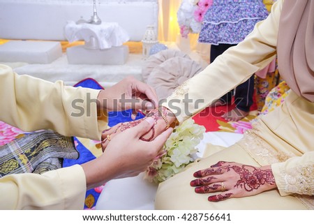 malay wedding groom bolstering bracelet gold ring on bride's finger, hand
