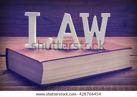 Wooden Human Figurine With  Judges Or  Auctioneer Gavel In Hand Sit On Red Book On The Rough And Grunge Wooden Table, Close Up, Front View, Effects
