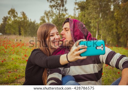 Couple doing silly and funny faces while taking selfie picture with their mobile phone in field of red poppies.