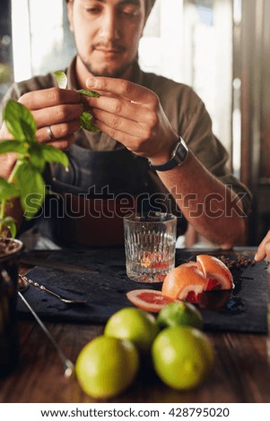 Cocktail preparation ingredients on table with bartender holding basil leaves.